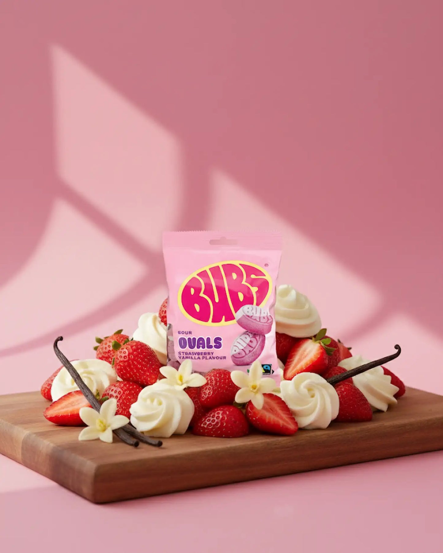 BUBS Swedish candy ovals - sour strawberry vanilla bag on a cutting board with strawberries and vanilla with pink back drop
