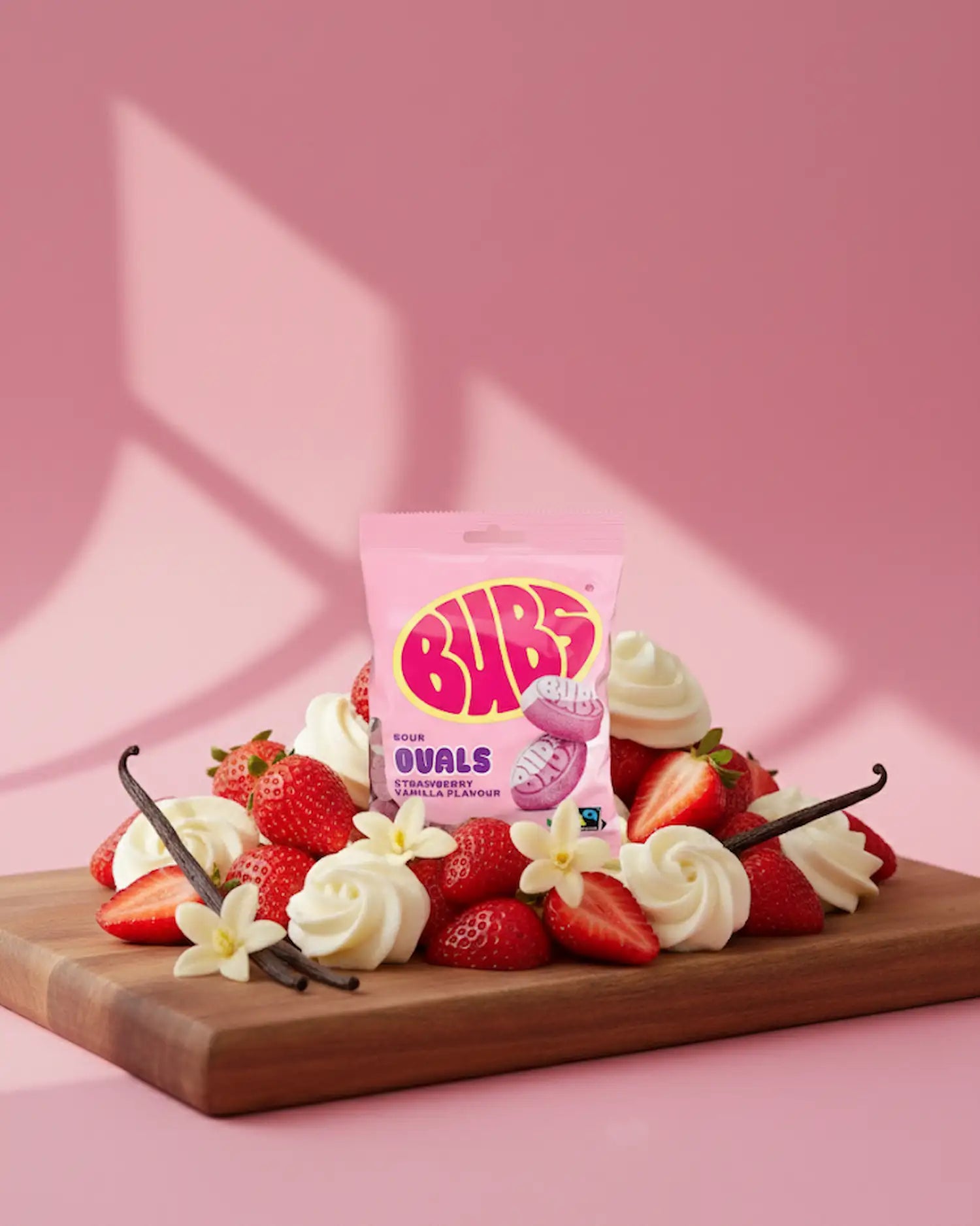 BUBS Swedish candy ovals - sour strawberry vanilla bag on a cutting board with strawberries and vanilla with pink back drop